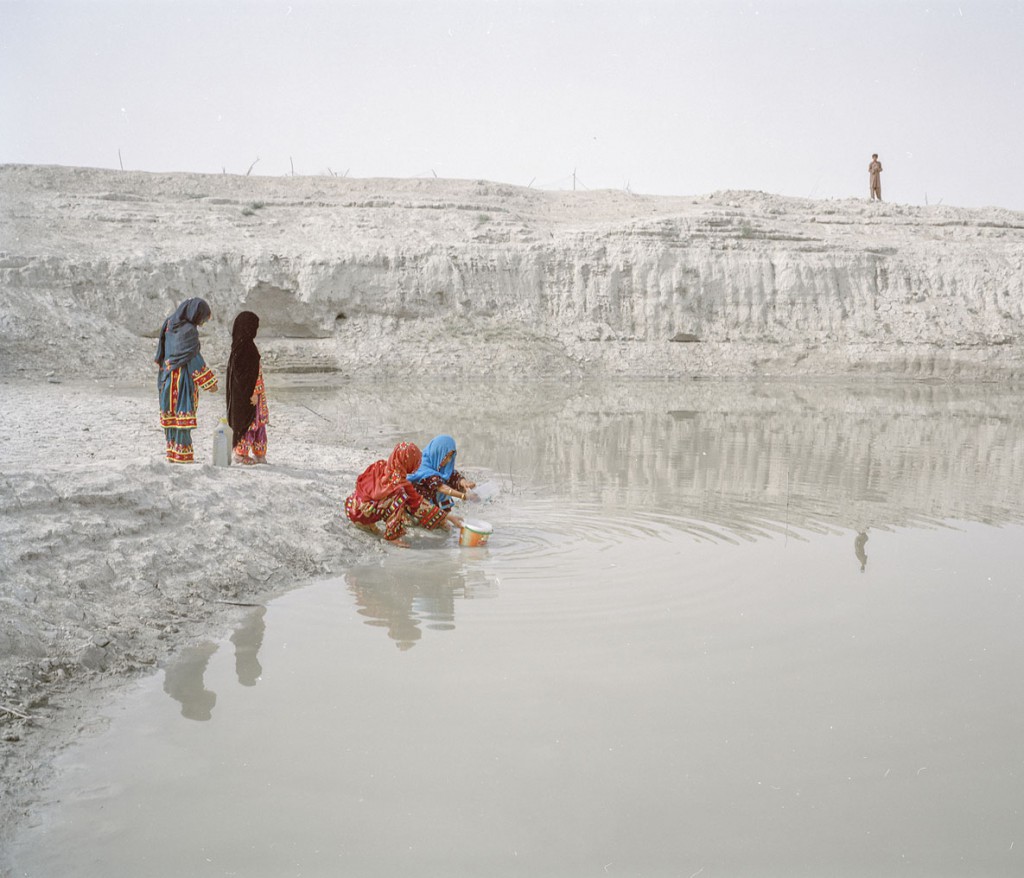 هاشم شاکری. از مجموعه‌ی Elegy for the Death of Hamun چهار دختر از یک خانواده در روستای چوتانی در حال جمع کردن آب از «هوتاگ» (چاله‌ای که آب باران در آن جمع می‌شود). طی دوران خشکسالی، این چاله‌ها کثیف و گل‌آلود می‌شوند، با این حال آنها تنها منبع آب در دسترس بسیاری از مردم هستند. آنها چاره‌ای جز این ندارند که این آب‌ها را بجوشانند و بنوشند. 